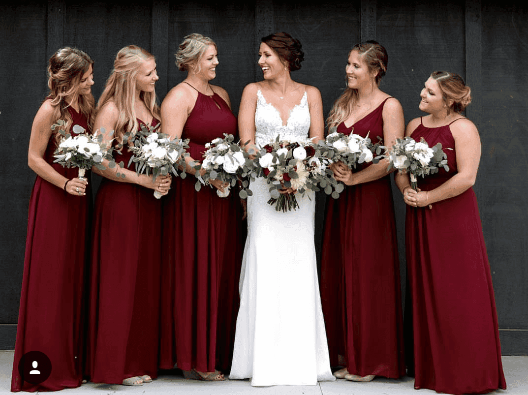 Bride in white gown with five bridesmaids in matching burgundy dresses holding bouquets.