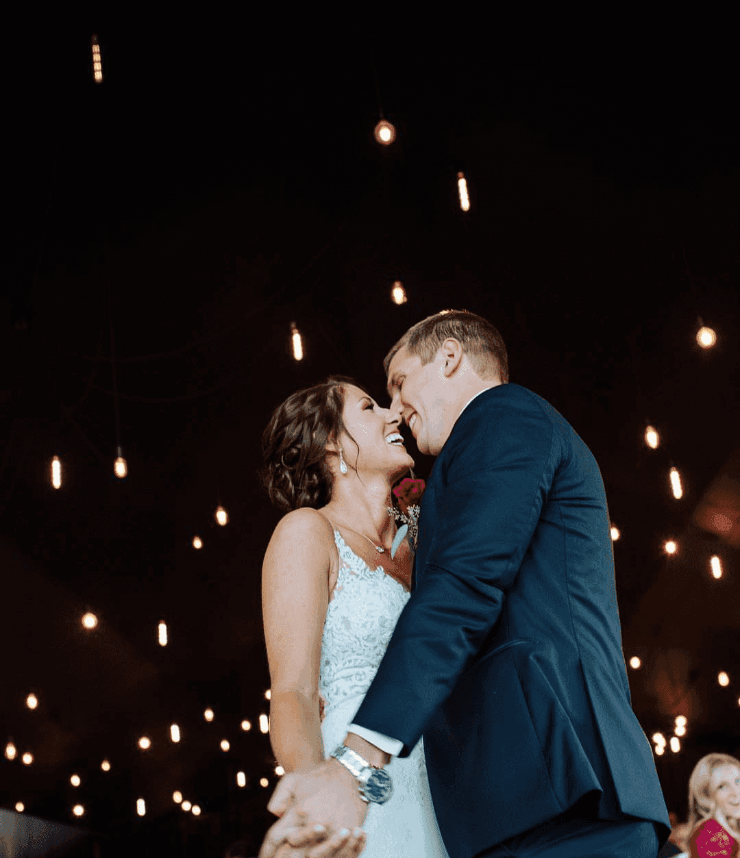 Bride and groom share a joyful first dance under hanging lights at their wedding reception.