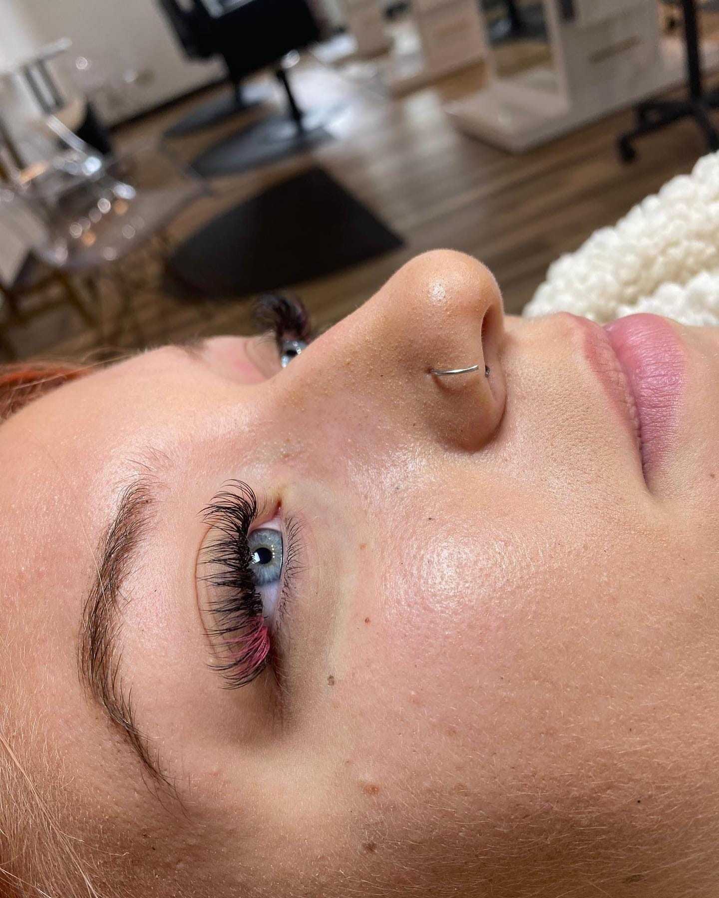 Close-up of a woman's face showing freshly done eyelash extensions in a salon setting.
