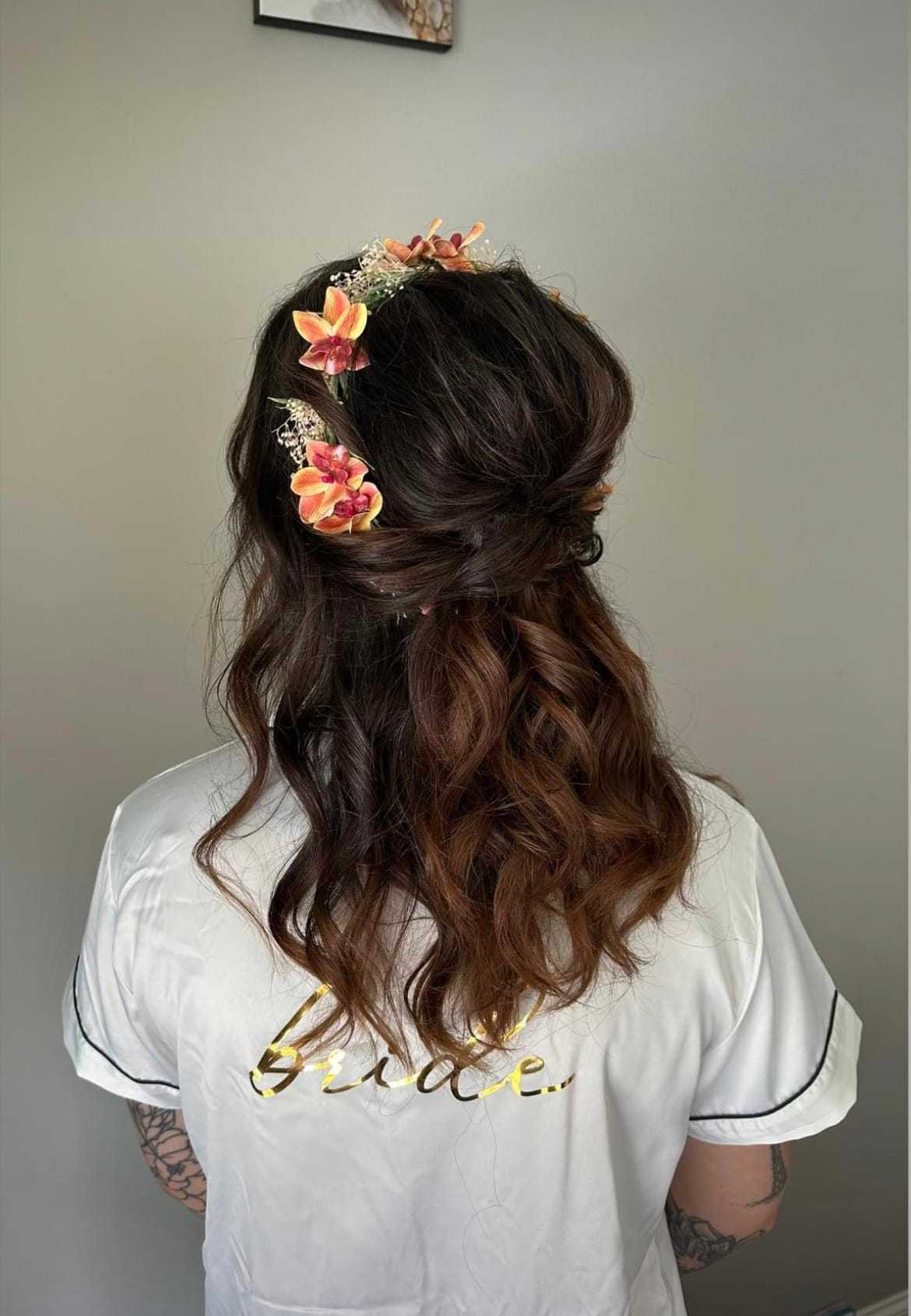 Bride with floral hair accessories and curled hair, wearing a white robe with "bride" on the back.